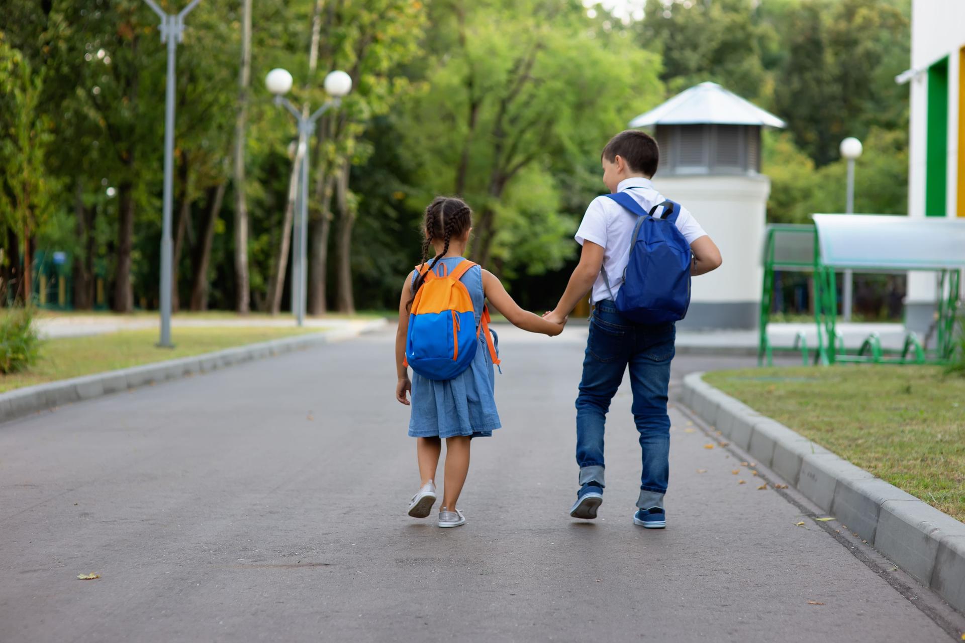 deux écoliers, une petite fille et un garçon avec des sacs à dos courir sur le chemin de la rue verte