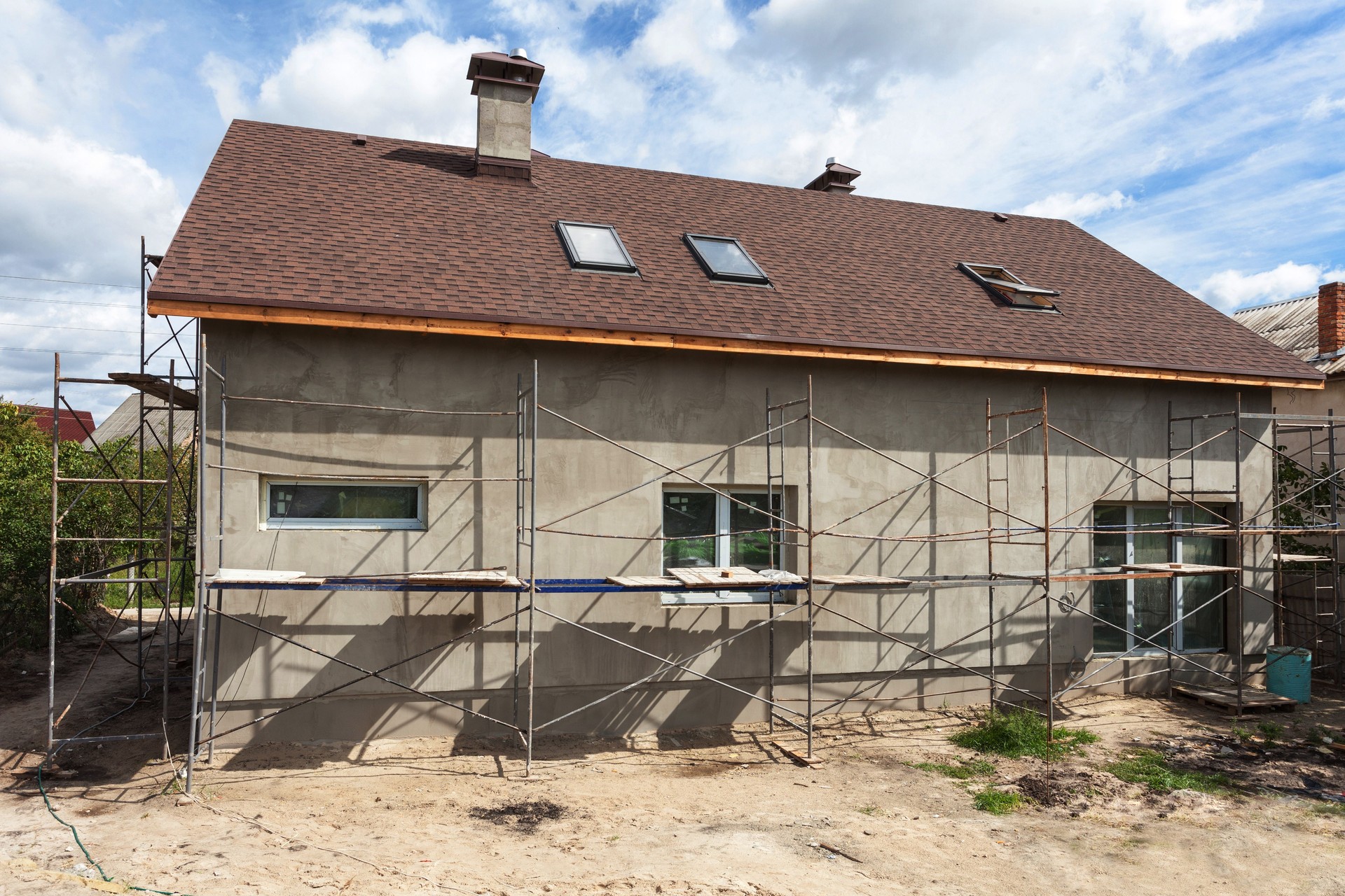 Construction ou la réparation de la maison rurale avec eaves, fenêtres, cheminée, isolation, toiture, façade, plâtrage des murs de fixation. Vue extérieure d’une maison neuve en construction et peinture. Plâtrage des murs extérieurs d’une maison de deux étages Neuve