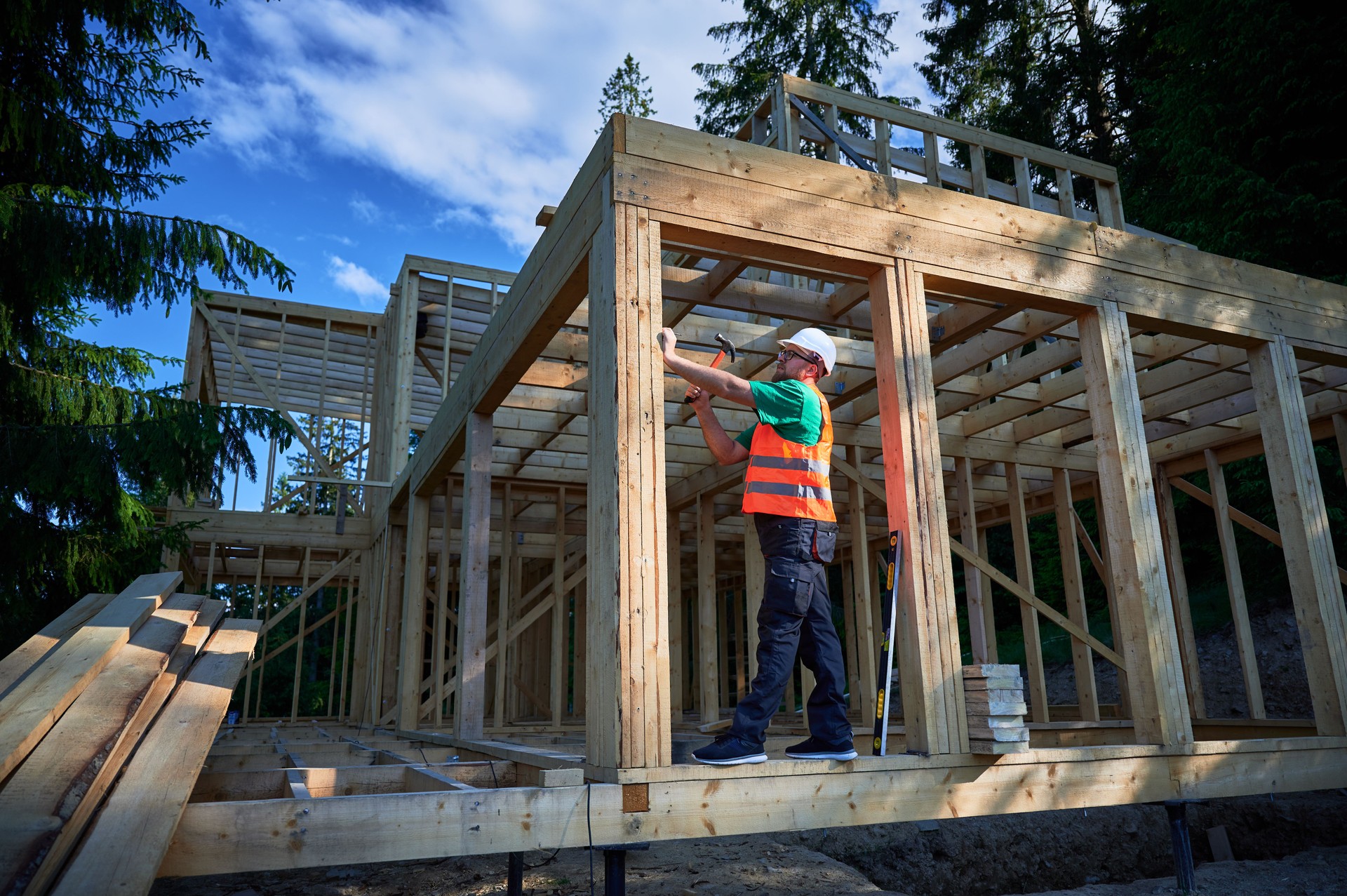 Charpentier martelant un clou tout en construisant une maison à ossature de bois de deux étages près de la forêt.